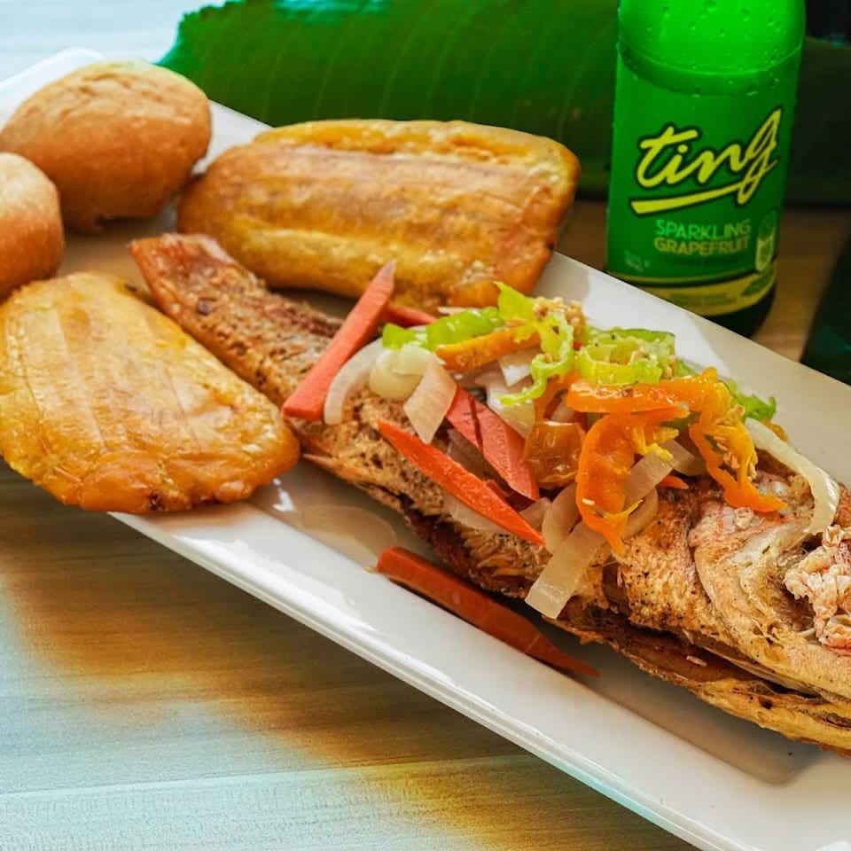 Loaded sandwiches with shredded lettuce, tomatoes, onions, and carrots beside bread rolls and a green grapefruit soda.
